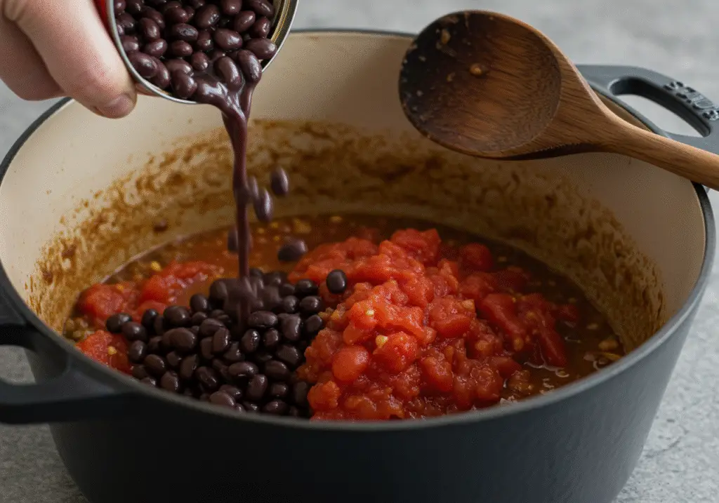 Pouring black beans and tomatoes into the pot for Sweet Potato Black Bean Chili preparation.