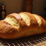 Freshly baked miche bread loaf cooling on a rack, highlighting its golden crust and delicious aroma in a rustic kitchen.