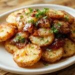 A plate of golden-brown, crispy breakfast potatoes arranged in a rustic skillet, topped with chopped herbs and sprinkled with seasoning, with a side of fresh garnish and a drizzle of sauce.